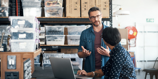 A man talking to a woman who is sitting at a desk on a laptop